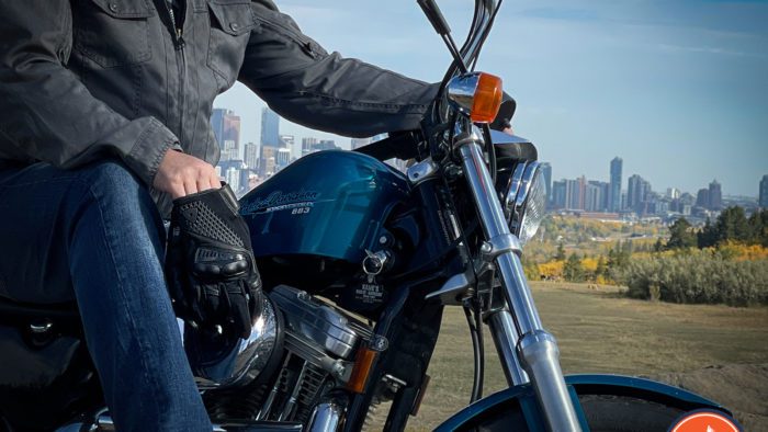 A reviewer trying out the Rev'it Echo Gloves in a glamour shot, riding a 1995 Harley Davidson and featuring a 883 Sportster Hugger and Joe Rocket Jacket.